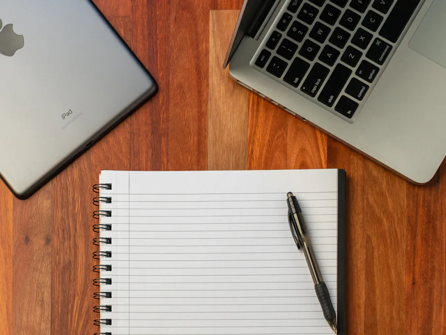Cuaderno de anillas en blanco junto a un portátil y una tableta sobre una mesa de madera